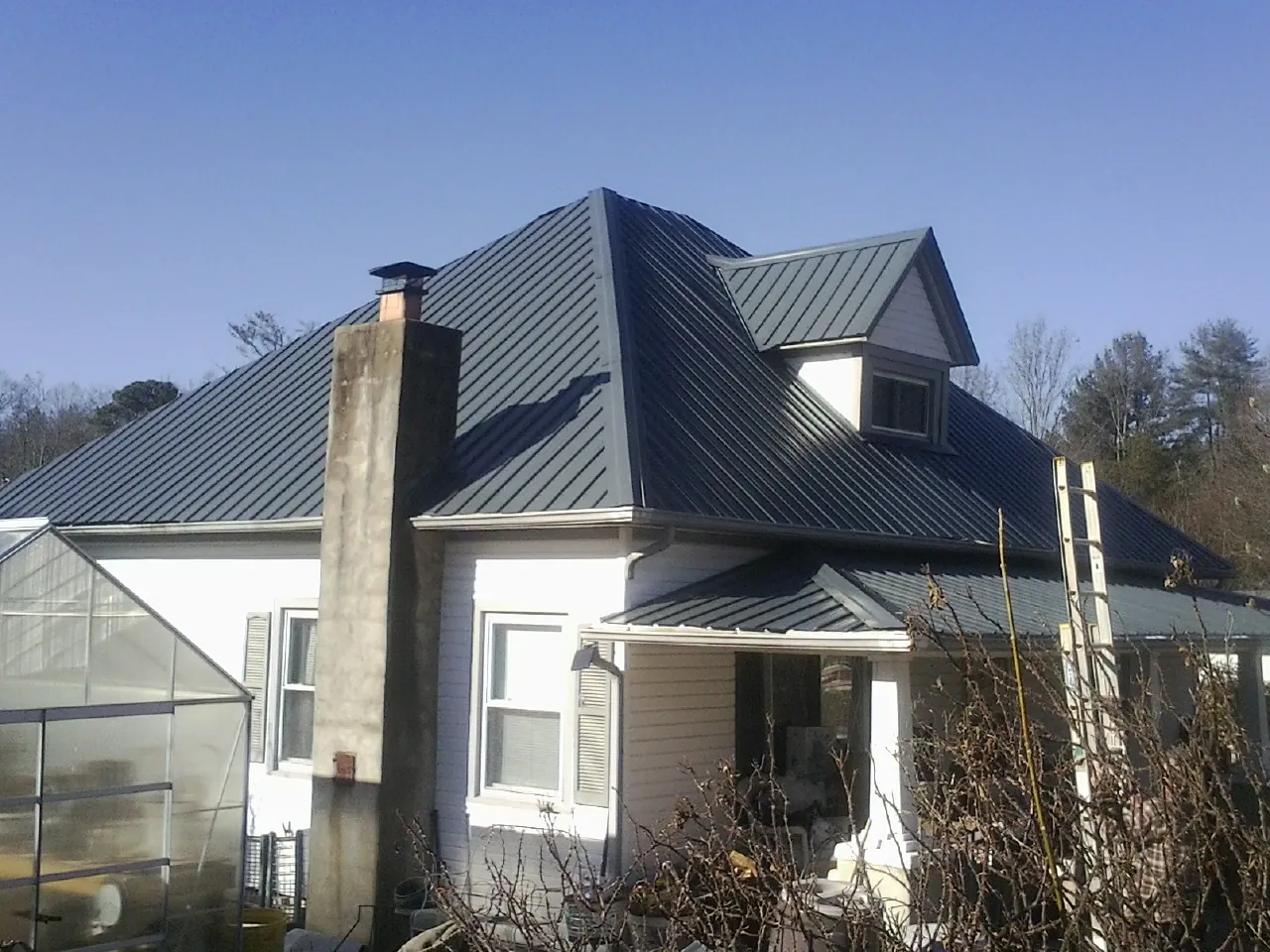Dark blue standing seam metal roof on a white farmhouse with dormer — Slate & Tile Roof Repair by Roofing Brothers in Belle Glade