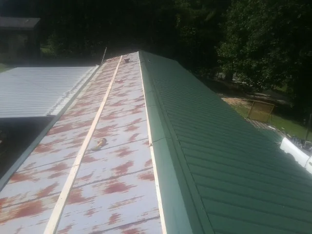 Old rusted panels beside newly installed green metal roofing — Wind Damage Roof Repair by Roofing Brothers in Belle Glade