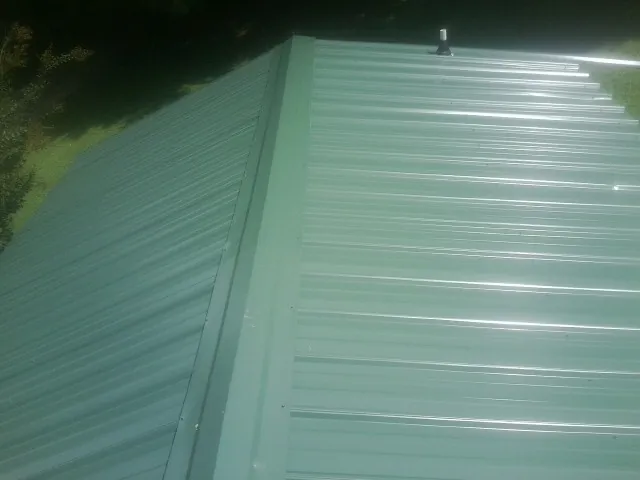 New green metal panels meeting at the ridge of a roof — Flat Roof Repair work by our crew in Belle Glade
