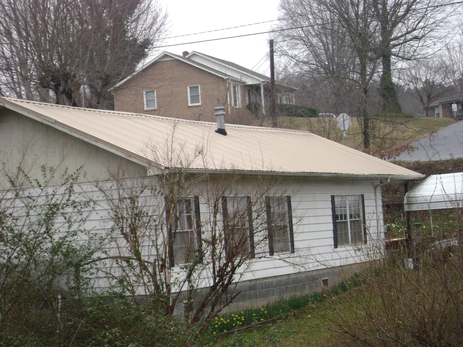 Tan metal roof on a white sided house set into a hillside — Commercial Roofing by Roofing Brothers in Belle Glade