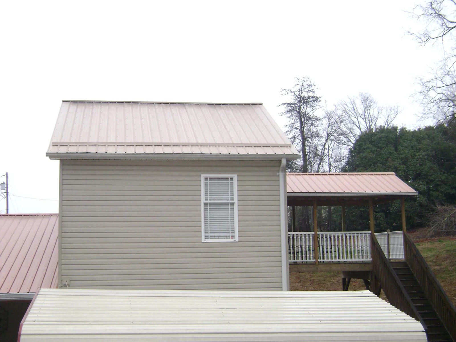 Tan metal roofs on a two story addition and attached porch, from a Roof Replacement job in Belle Glade
